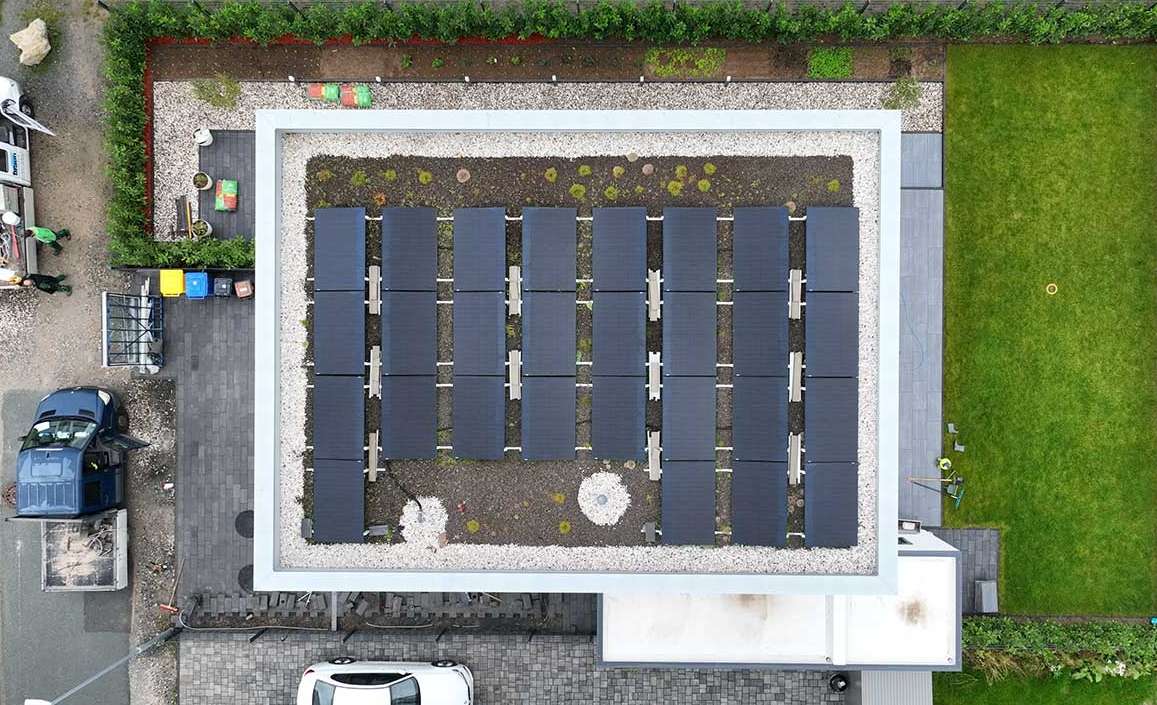 Top-down view of a modern residential rooftop solar PV system installed on a flat roof, surrounded by garden and parking, showcasing clean energy adoption in home settings