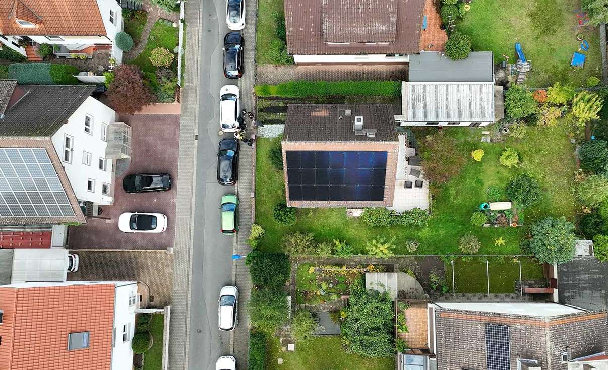 Top-down view of a residential solar rooftop system installed on a red-brick house in a German neighborhood, highlighting clean energy adoption in family households